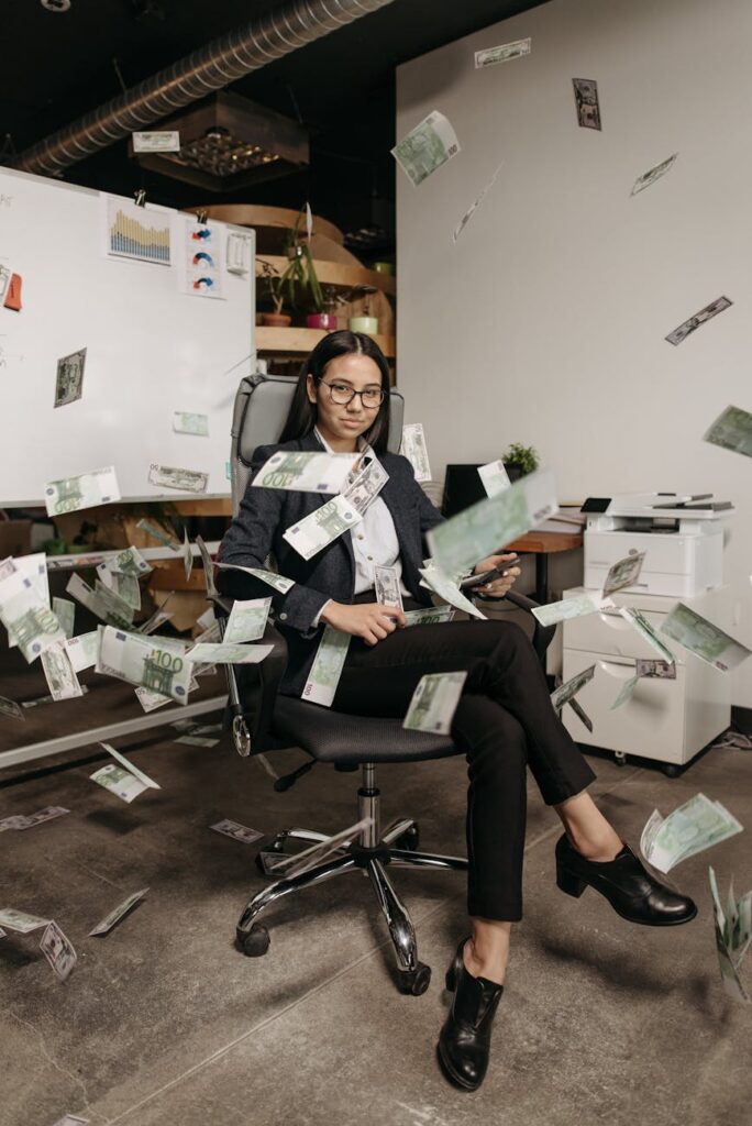 woman sitting on an office chair with money flying all around her